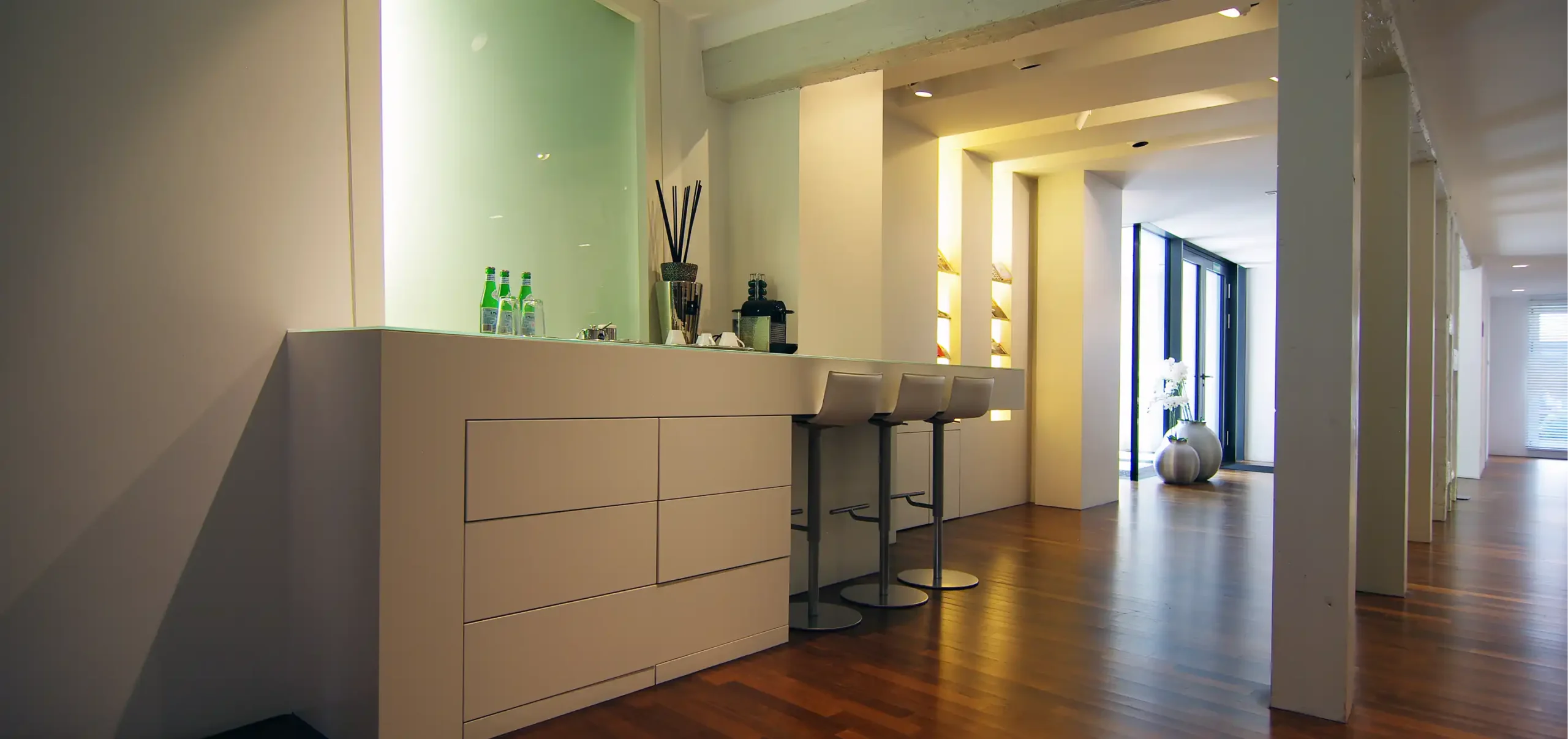 Theke mit Hochstühlen, Lichtdesign, indirekte Beleuchtung in Wandnischen erzeugt Tiefe und Orientierung, Empfangsbereich, Theke, Holzdielen, Zahnarztpraxis Krauch, Stadt:Ulm