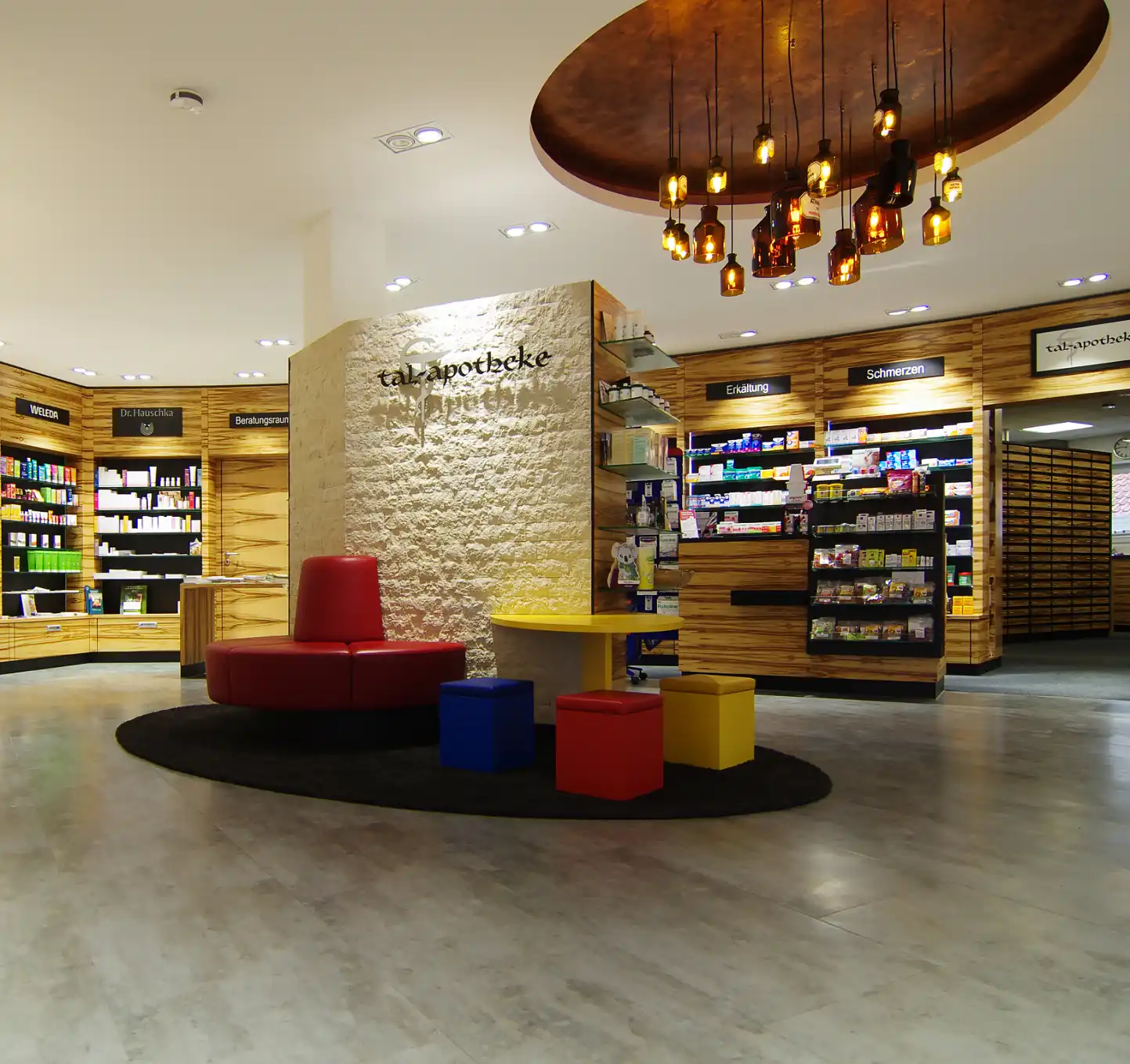 Tal Apotheke in Deggenhausertal: Offizin mit Holzregalen, Natursteinwand und farbigen Sitzinseln