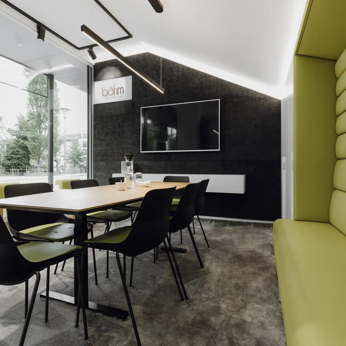 Büroflächen Böhm, Raumkonzept, Abgeflammte, gerissene Holzverkleidung in Schwarz mit indirekter Beleuchtung und Monitor, 
Konferenztisch mit Bestuhlung,
integrierte platzsparende Sitzbereiche, Sitzpolster in grün,
Akustikdecke und graugrüne Teppiche zur Klangoptimierung