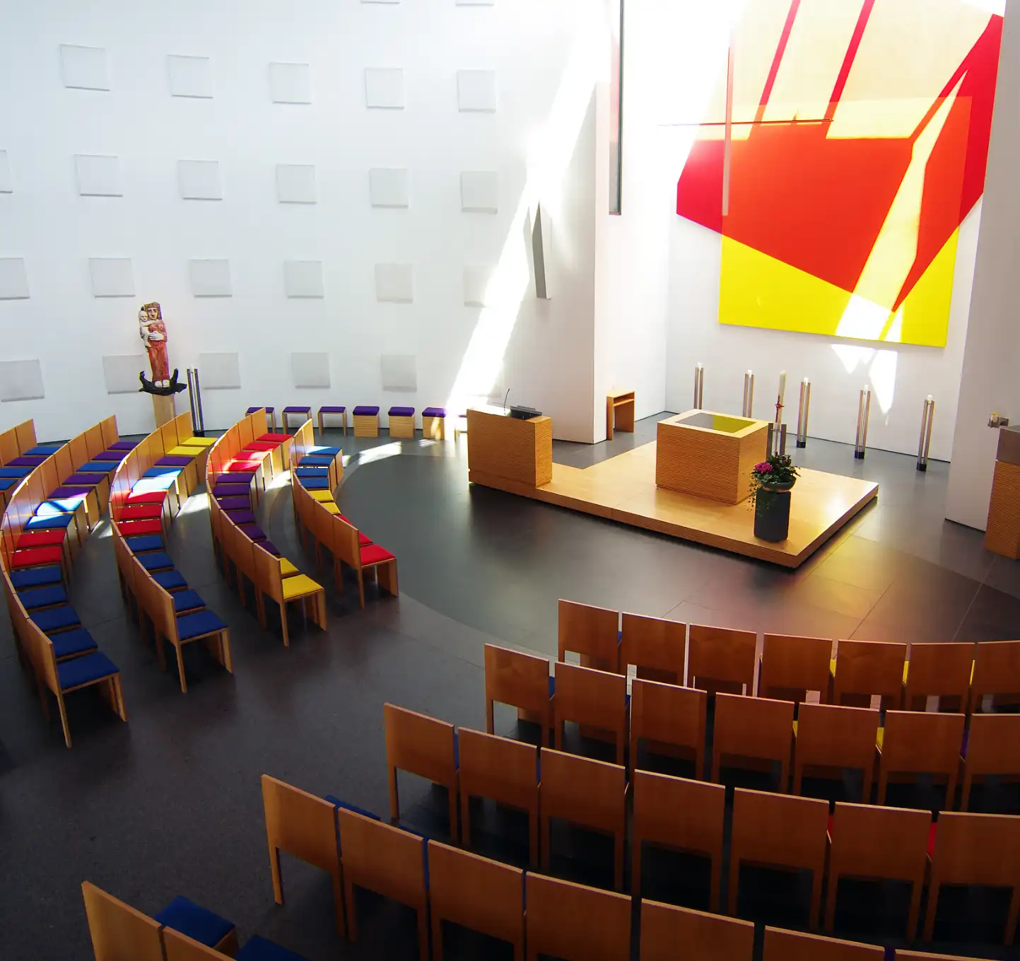 Kirche St. Klara in Ulm, Innenraum,  Kirchenschiff, Gebetsraum, Weise Wände, schlichter Holzaltar leicht erhöht auf einen Holzpodest, indirekte Tageslicht Beleuchtung der Altar Nische, kreisförmige Anordnung der Bestuhlung, Holzstühle mit Fingerzinkenverbindung    

