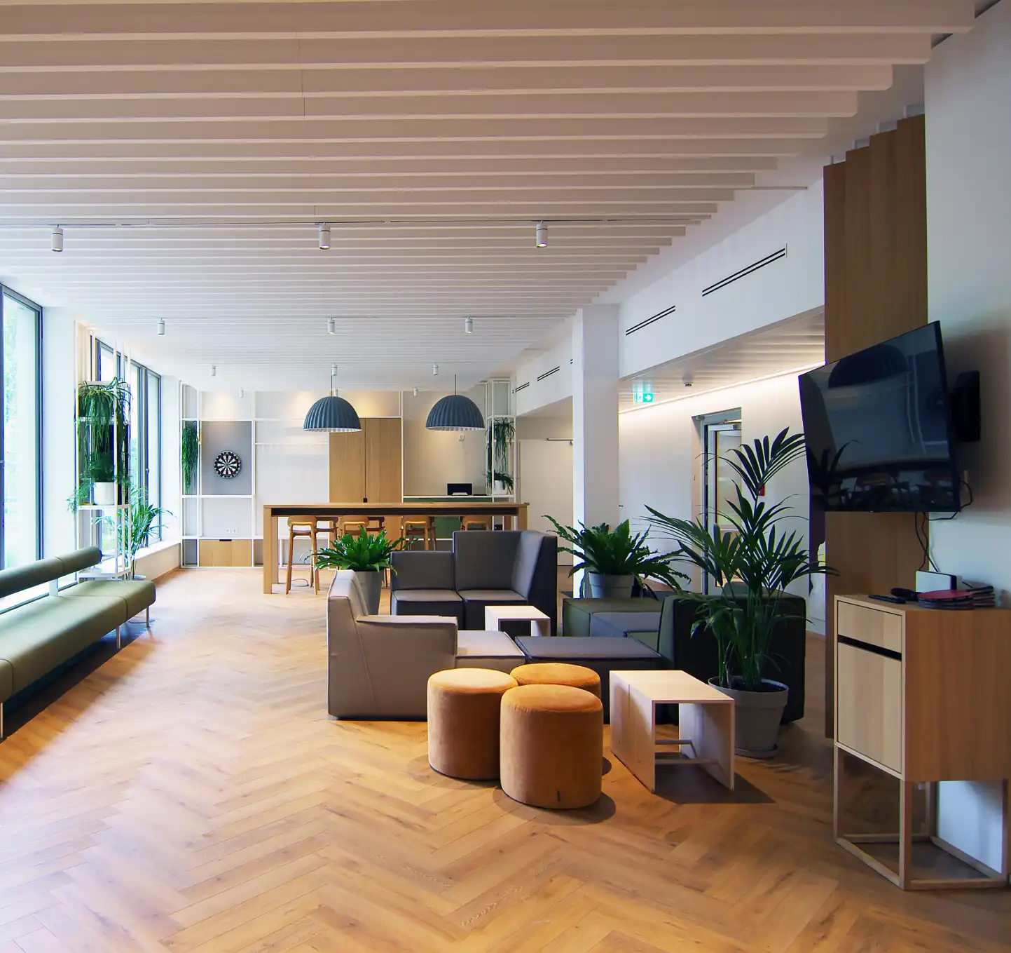 Büroräume von Bloom Offices, inklusive Selbstbedienungsküche und Tischtennisfläche, Fenster, Sitzbereich mit Polstermöbel, Hochtisch mit Bestuhlung, Holz, Stahl und frische Grüntöne, funktionale und Elemente aus schlichter Eiche, weiße Stahlregale und frische Grüntöne 
,Stauraummodule mit Dartscheibe, Playstation.  Innenausbau der maßgeschneiderte Möbellösungen bietet