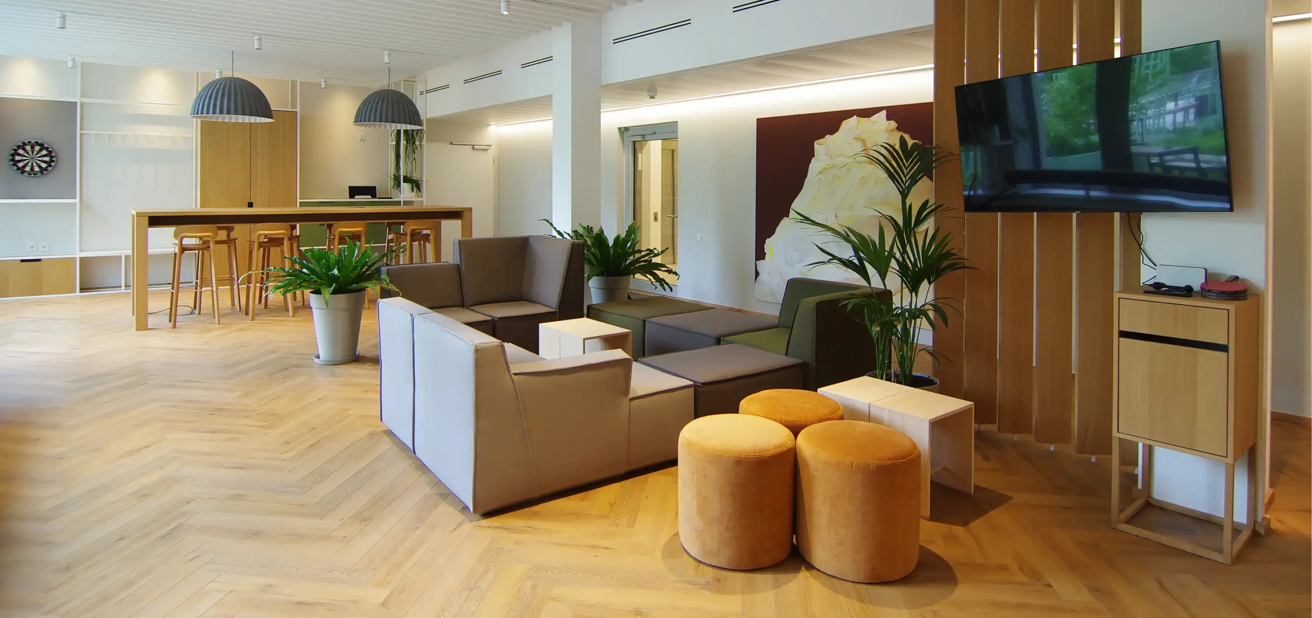 Büroräume von Bloom Offices, Fenster, Sitzbereich mit Polstermöbel, im Hintergrund Tisch mit Bestuhlung, Hängelampen grau weiß, weiße Stahlregale und frische Grüntöne
