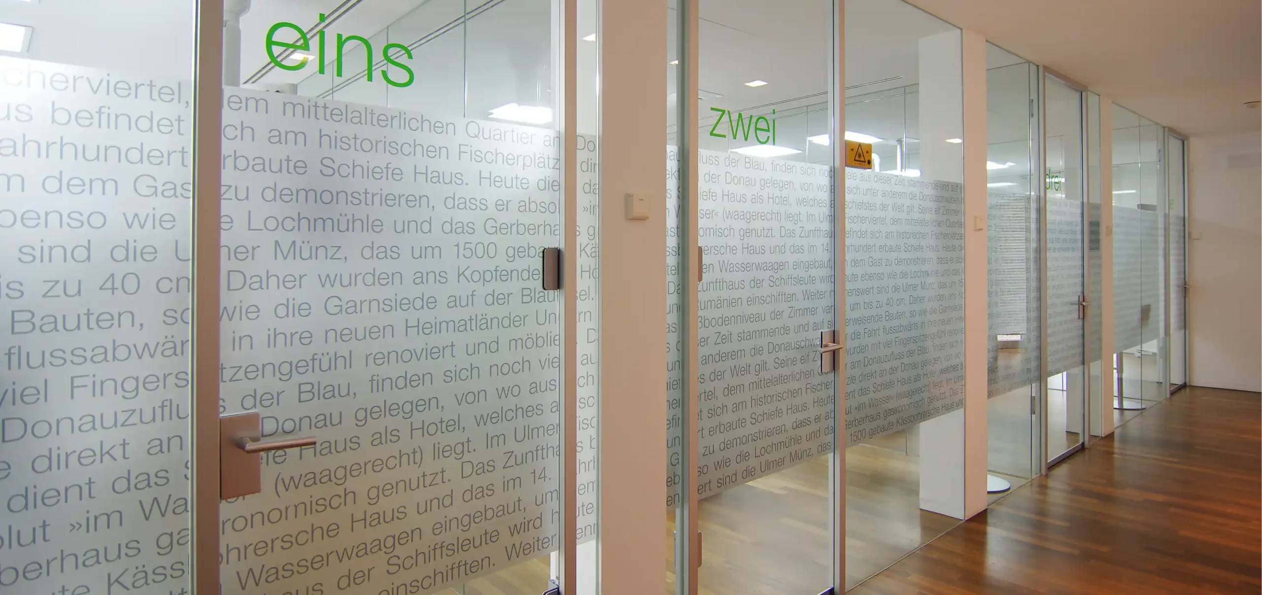 Zahnarztpraxis Krauch, Behandlungszimmer, Glastür mit Sichtblende, dunkler Naturholzboden, helle Auleuchtung