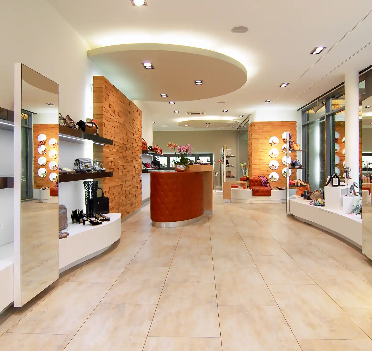 Verkaufs- und Ladenfläche von Unglaublich Schuh, 
Spaltholzwand aus Eiche mit schwebender Optik, abgehängte Decke über dem Tresen mit indirekter Beleuchtung, Tresen gestepptem Echtleder und Metallabschlussborde,
Spiegel, Wandverblendungen aus Holzsegmenten, Accessoires und Schuhe auf Hochglanzregalen