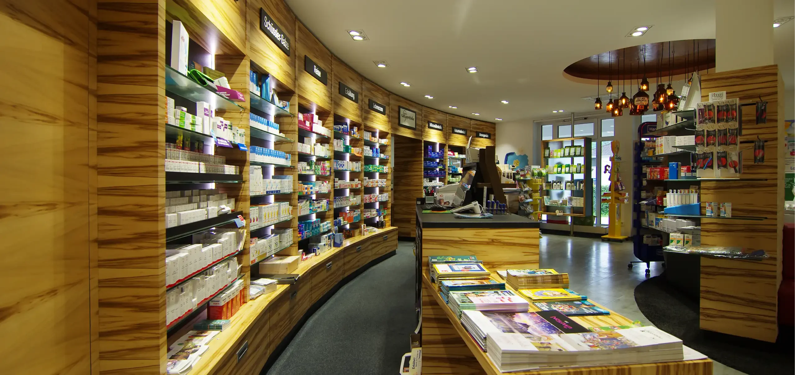 Andere Perspektive vom Verkaufsraum Tal Apotheke, Verkaufstresen mit Fokus auf die Wandschränke und deren Unterschränke