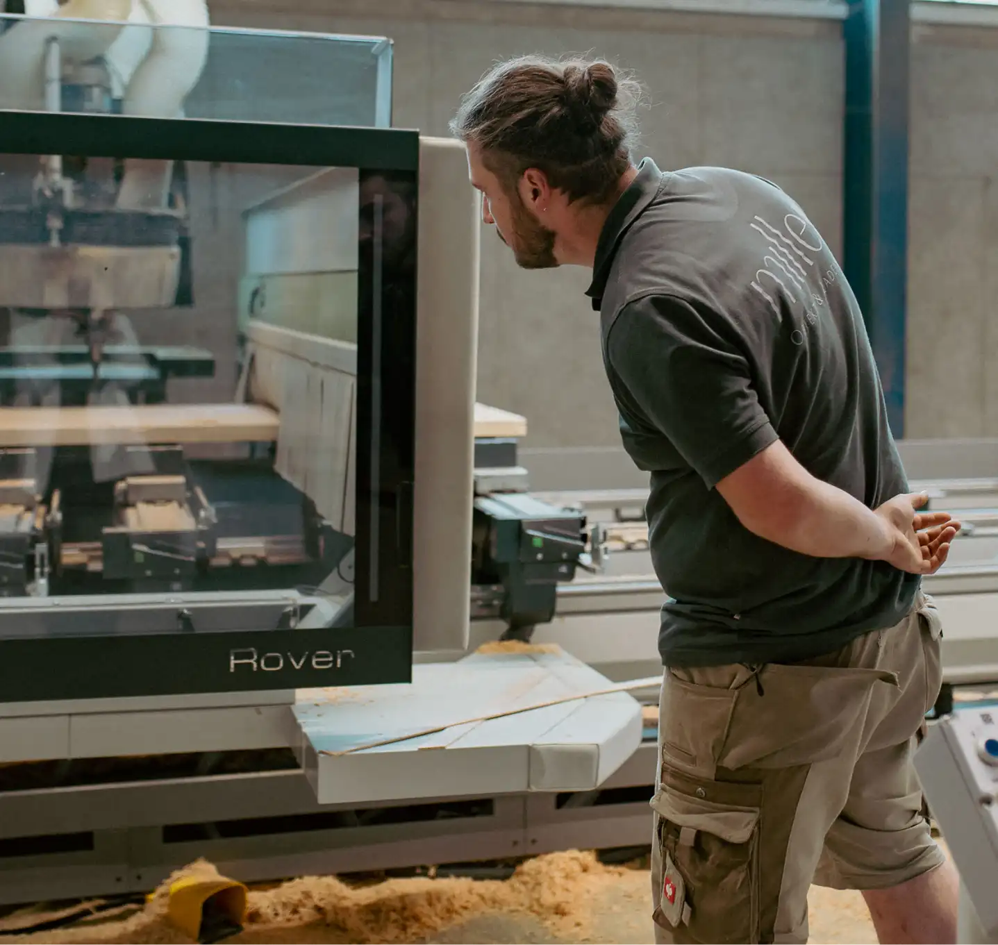 Produktionsraum, Mitarbeiter an der CNC - Maschine mit Sichtfenster, Überwachung der millimetergenauen Fertigung von der Holzkonstruktion