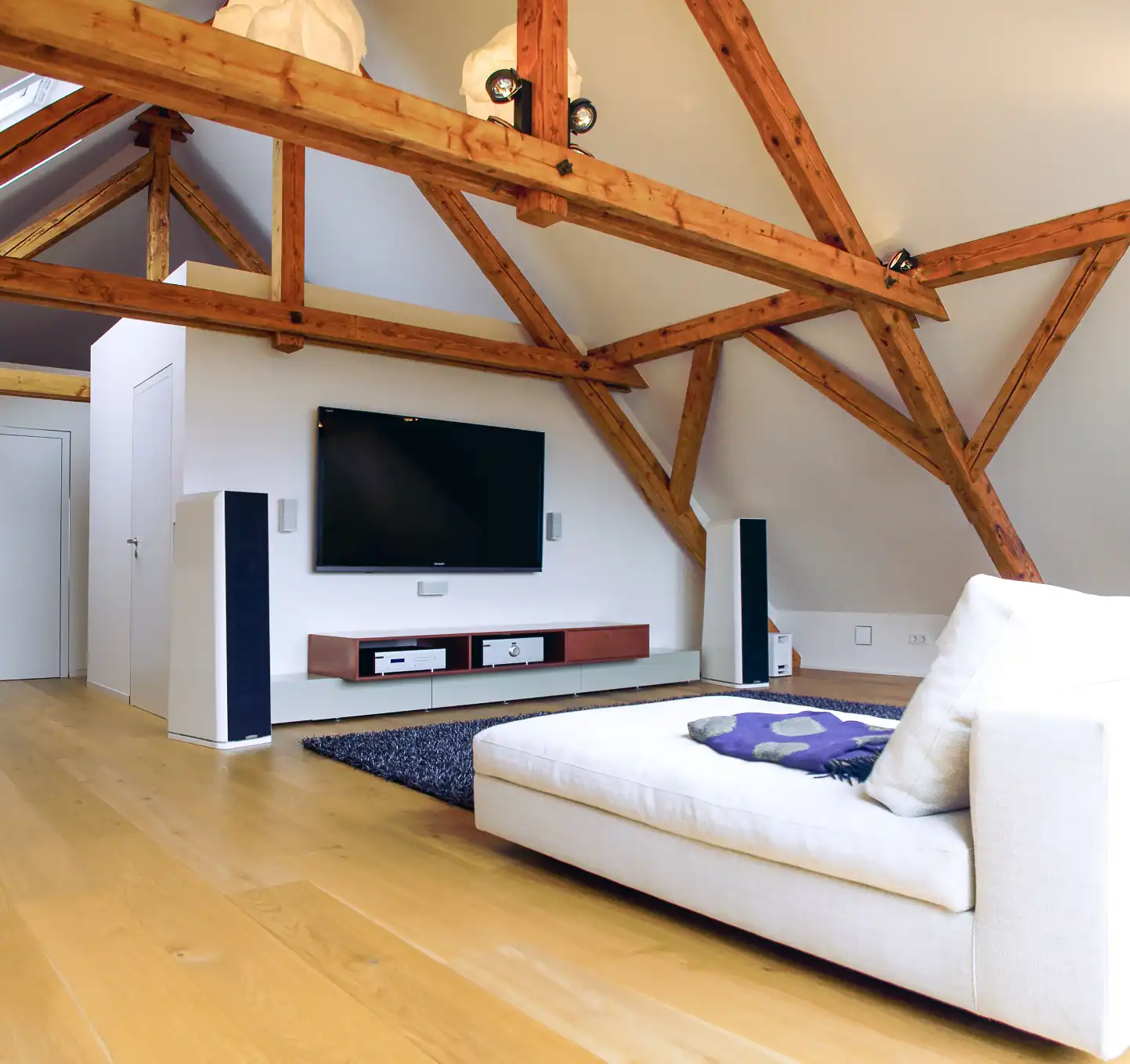 Ausbau eines Bestandsgebäude, Wohnzimmerbereich mit Dachschrägen und freistehendes Gebälk, 
mit Heimkino und Sofa, 
rechts und links Boxen, 
Sideboard mit Boxen


