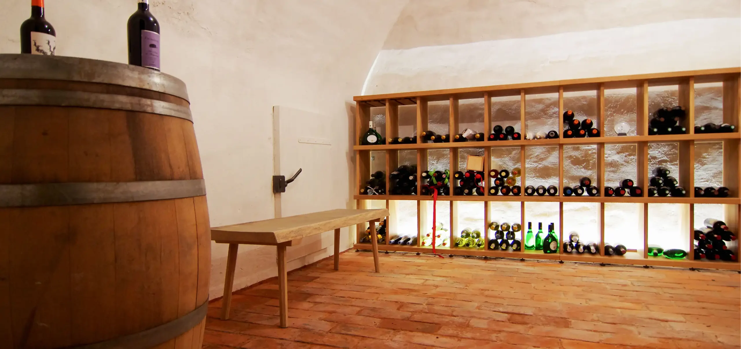 Weinkellergewölbe, Weinfass, Weinregal aus Holz gefertigt, indirekte Beleuchtung des Weinregal, schlichte Holzbank, Ziegelboden