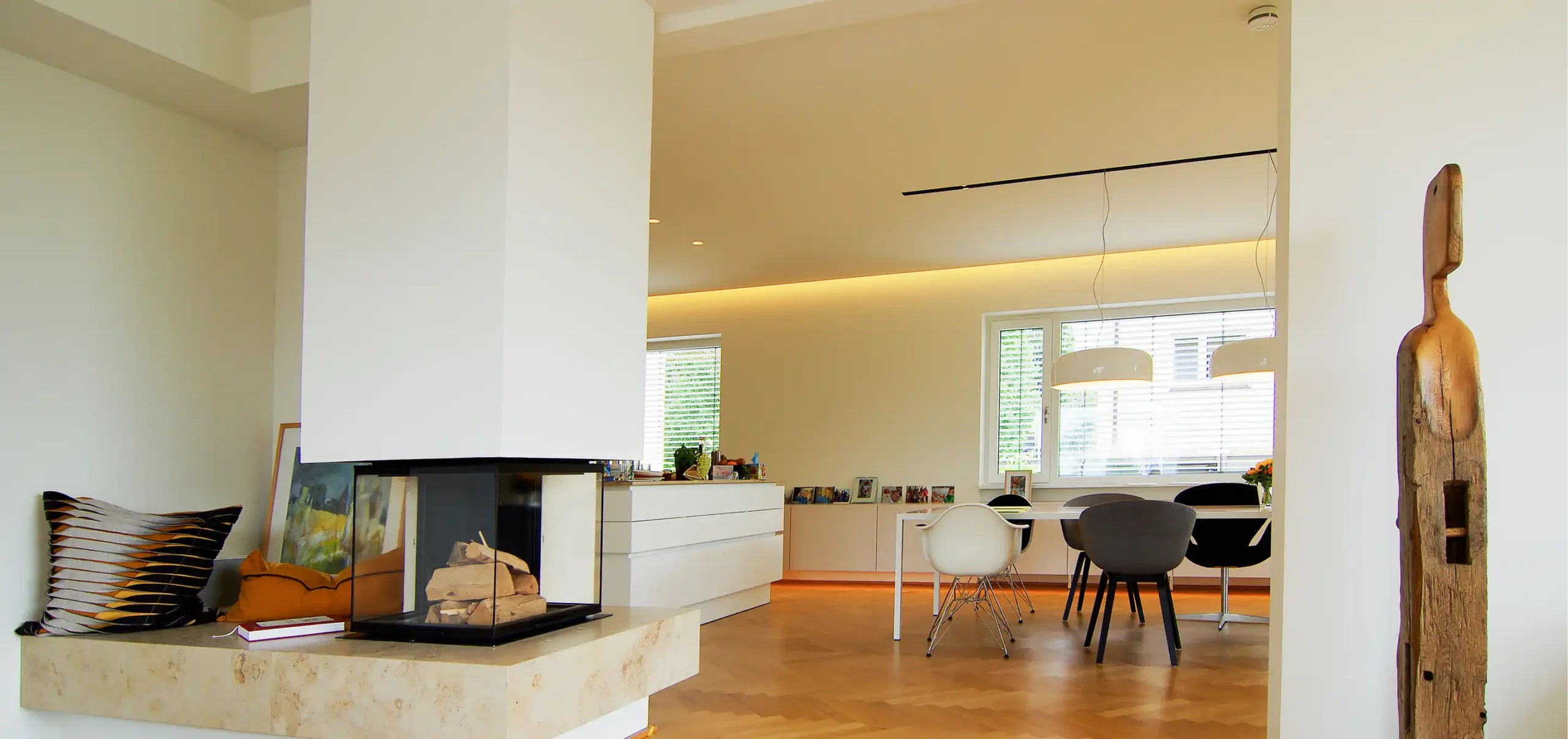 Wohnzimmerbereich mit Kamin, Tisch und unterschiedliche Designer - Stühle, Hängelampen über den Tisch, weiße Sideboards
