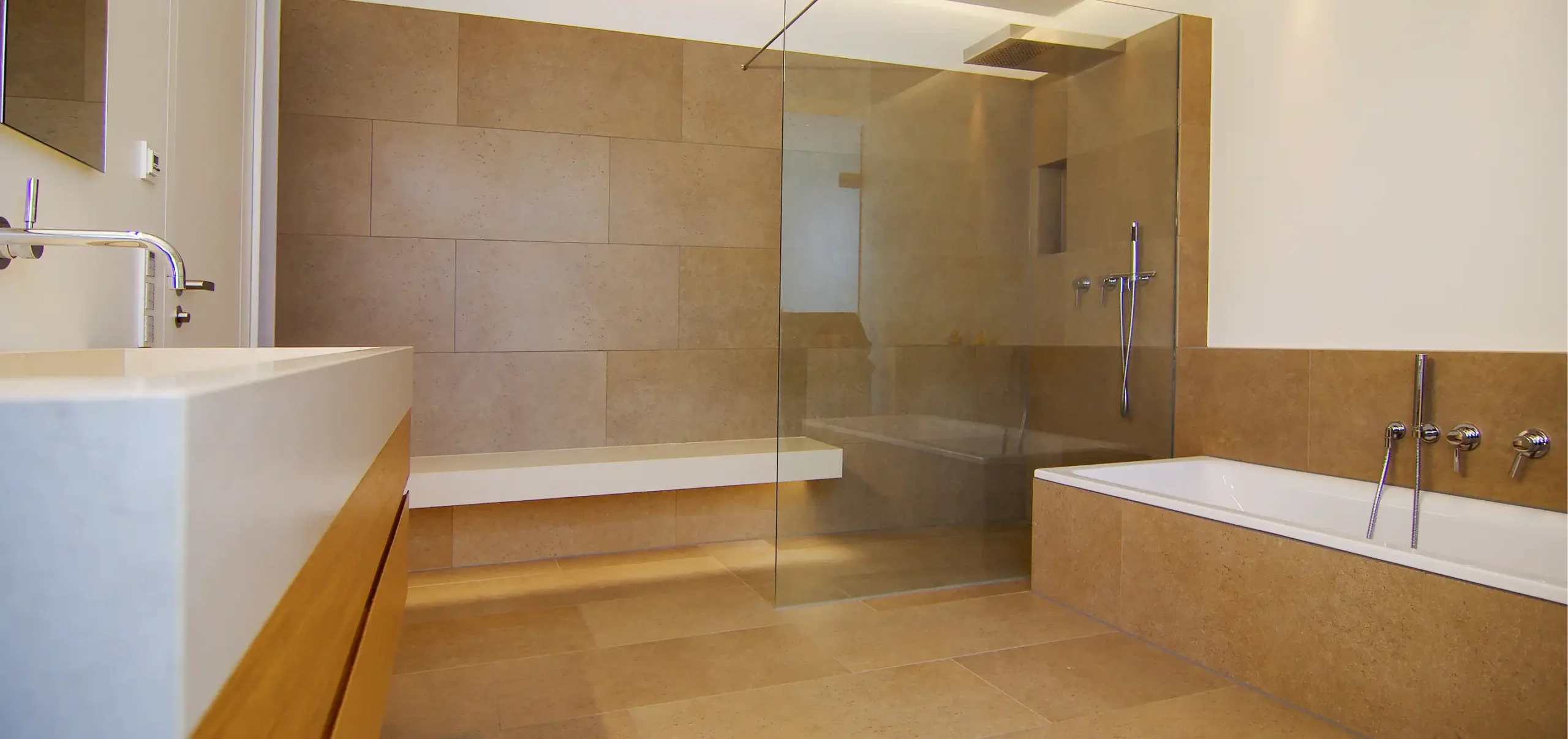 Badezimmer, links Waschbecken mit Holzunterschrank, rechts Badewanne, hinten Duschbereich mit Glasabschirmung