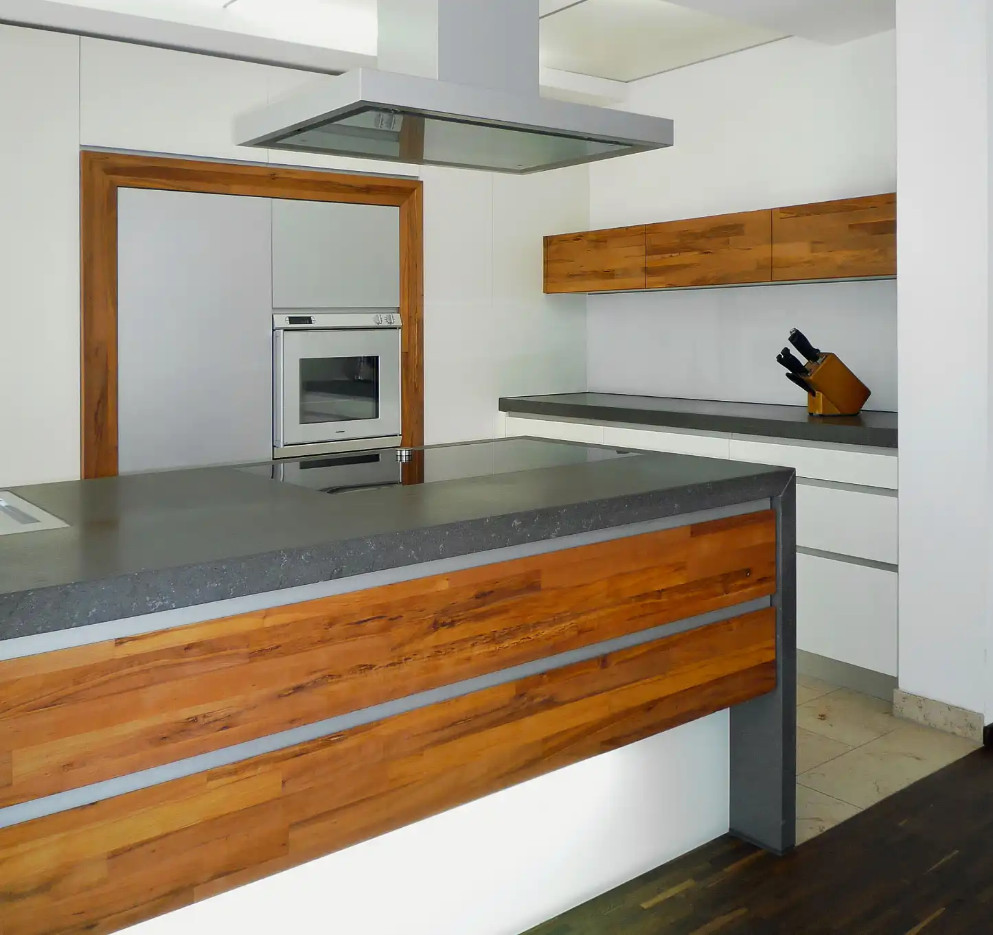 Küche mit Natursteintresen, Abzugshaube mittig im Raum, Herd und Schrank maßgefertigt in die Wand eingebaut